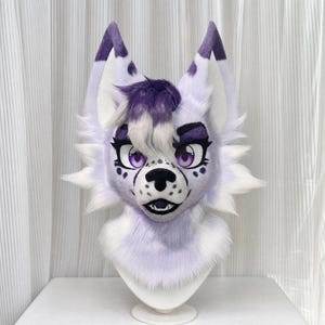 May include: A furry wolf head with a purple and white color scheme. The head has large, expressive purple eyes, a black nose, and a smiling mouth. The ears are pointed with purple accents. The fur is soft and fluffy, creating a whimsical and playful appearance.