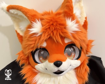 May include: A vibrant orange and white fox fursuit head with large, expressive eyes. The head features fluffy fur, detailed ears, and a friendly expression. The fursuit is designed with a black backing.