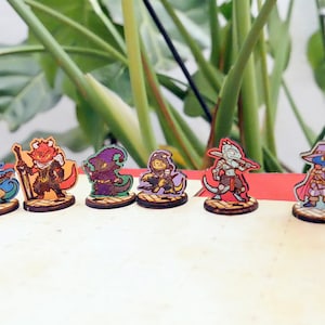 May include: Set of six miniature fantasy character figurines, each painted with vibrant colors and detailed features. The characters include a lizard person, a dragon, a wizard, a rogue, a cleric, and a bard. Each figurine is mounted on a wooden base.