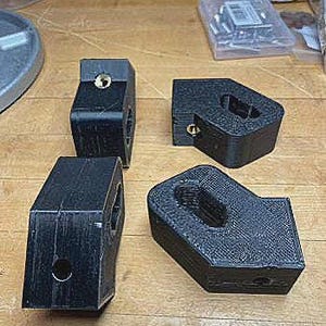 Op de afbeelding: Vier zwarte 3D-geprinte kunststof beugels met een getextureerd oppervlak. Elke beugel heeft een rechthoekige vorm met een centrale opening en een kleine ingebedde messingkleurige metalen schroefdraadbus aan één zijde voor bevestiging.