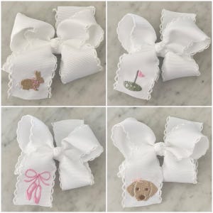 May include: Four white grosgrain ribbon hair bows with scalloped edges. Each bow features a unique embroidered design: a tan bunny with a pink collar, a golf hole with a pink flag, a pair of pink ballet slippers, and a tan dog with a pink bow.