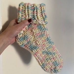 Puede incluir: Un par de calcetines de punto coloridos en tonos rosa, azul y amarillo. Los calcetines están hechos con un hilo grueso y tienen un puño de canalé.