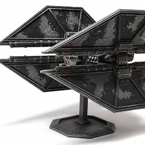 Puede incluir: Modelo detallado de una nave espacial TIE fighter negra y gris, con paneles solares angulares y detalles mecánicos intrincados. El modelo está montado sobre un soporte negro, mostrando el diseño icónico de una franquicia de ciencia ficción.