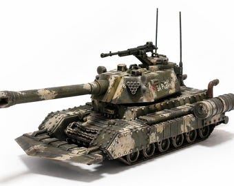 May include: A scale model tank featuring a green and tan camouflage pattern, a long main gun barrel, a mounted machine gun on the turret, and two antennas. The side of the turret displays a triangular emblem and the Cyrillic text ZA RODINU.