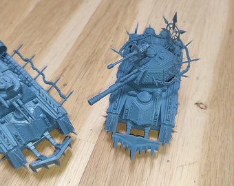 May include: Two gray plastic model tanks with spikes and chains. The tanks are on a wooden surface.