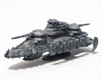 May include: A gray and black model of a futuristic tank with multiple turrets and a spiked front. The tank has a camouflage pattern and is set against a white background. It appears to be a miniature collectible.