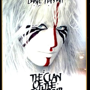 以下が含まれることがあります： 映画「The Clan of the Cave Bear」のポスター。ダリル・ハンナが出演。白い顔ペイント、黒い模様、赤いストライプが特徴。タイトルと「Gold Collectors Edition」の文字が見える。