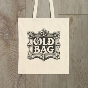 Peut inclure: Un sac fourre-tout en toile blanche avec du texte noir qui dit "OLD BAG" dans un cadre décoratif.