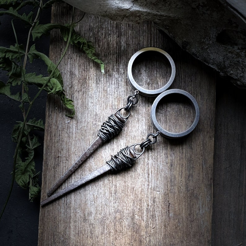 May include: Two silver hoop earrings with a wire wrapped around the hoops and a long, thin, silver wire attached to each hoop. The wire is wrapped around the hoops and then twisted into a point. The earrings are on a wooden surface.