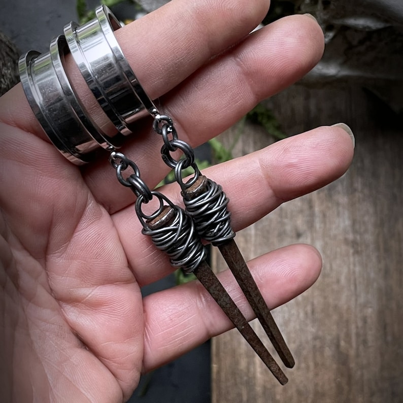 May include: A pair of silver earrings with a long, thin, wire-wrapped, rusty nail design.