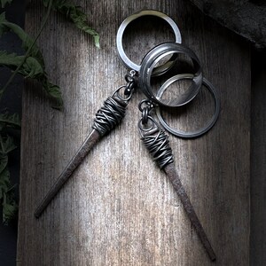 May include: A silver key chain with three interlocking rings and two dangling metal spikes wrapped in wire.