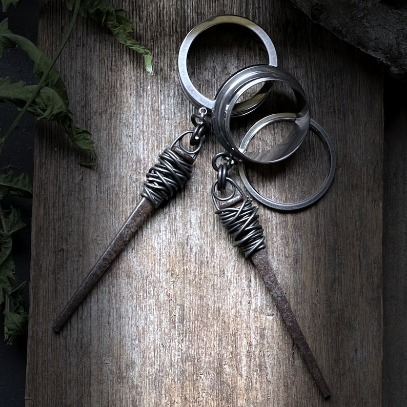 May include: A silver key chain with three interlocking rings and two dangling metal spikes wrapped in wire.