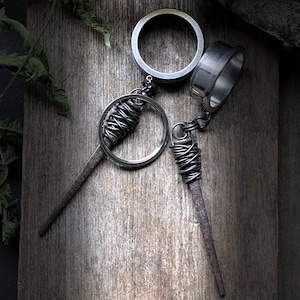 May include: Two silver metal earrings with a circular design and a dangling wire wrapped in a spiral. The earrings are on a wooden surface.