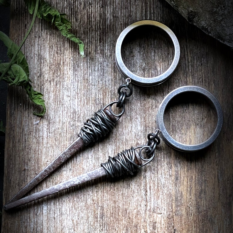 May include: Two silver metal rings with a twisted wire design attached to each other. The rings are connected by a chain and have a dark gray finish.