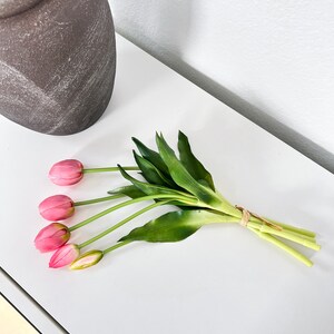 May include: A bouquet of pink artificial tulips with green stems and leaves tied together with a brown string.