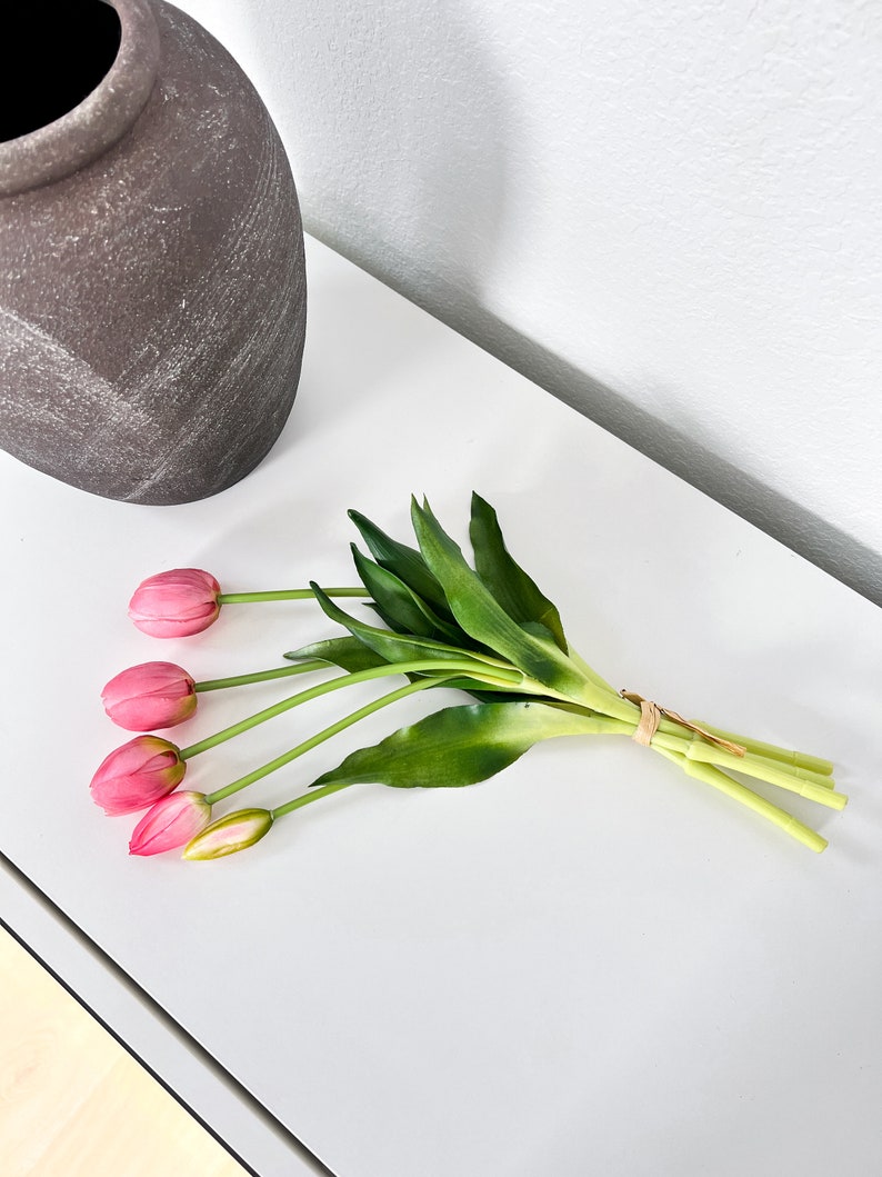 May include: A bouquet of pink artificial tulips with green stems and leaves tied together with a brown string.