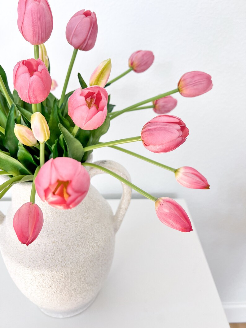 May include: A white ceramic vase with two handles, filled with a bouquet of pink tulips.