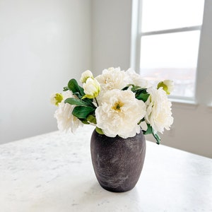 May include: A bouquet of white peonies in a dark gray ceramic vase on a white marble countertop.