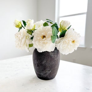 May include: A bouquet of white paper flowers in a dark gray ceramic vase on a white marble surface.