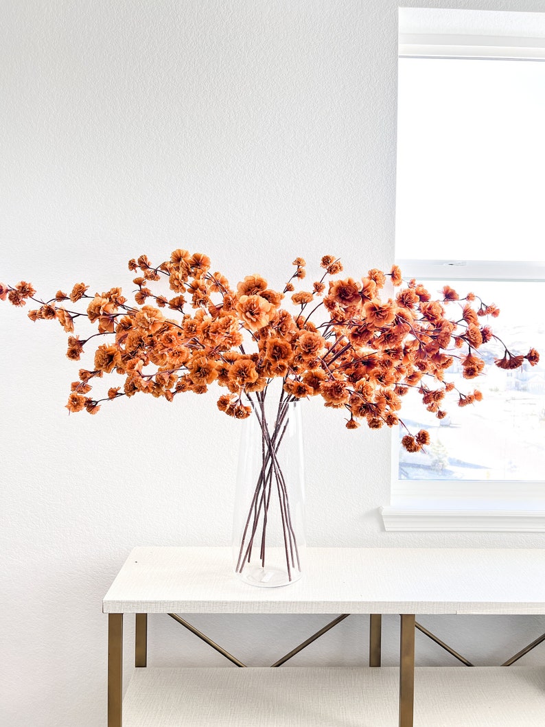 May include: A bouquet of dried orange flowers in a clear glass vase on a white table with gold legs.