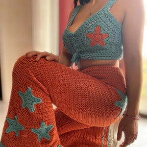 Puede incluir: Un conjunto de crochet de dos piezas con una parte superior azul y pantalones naranja. La parte superior tiene un diseño de estrella y los pantalones tienen varios diseños de estrellas.