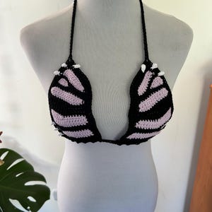Pode incluir: Top de biqu&iacute;ni de croch&ecirc; preto e lavanda em um manequim. O top com gola halter tem detalhes brancos e bojos listrados. O design feito &agrave; m&atilde;o &eacute; uma pe&ccedil;a de roupa de banho marcante.