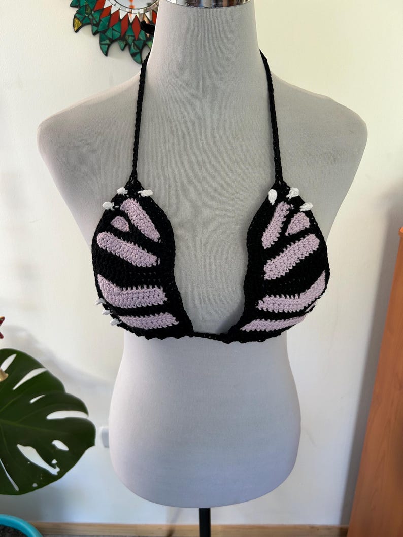 Pode incluir: Top de biqu&iacute;ni de croch&ecirc; preto e lavanda em um manequim. O top com gola halter tem detalhes brancos e bojos listrados. O design feito &agrave; m&atilde;o &eacute; uma pe&ccedil;a de roupa de banho marcante.
