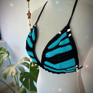 Pode incluir: Top de biqu&iacute;ni de croch&ecirc; preto e turquesa. O top apresenta um design de asa de borboleta com listras turquesas em um fundo preto. As al&ccedil;as e as bordas s&atilde;o pretas, com pequenos detalhes brancos.