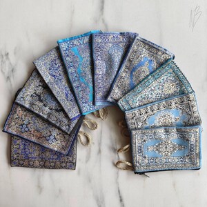 Könnte beinhalten: Ein Set aus zehn kleinen blauen Stofftaschen mit silbernen Mustern, Reißverschlüssen und goldenen Kordeln. Die Taschen sind in einem Halbkreis angeordnet, wobei die Kordeln aus der Mitte herausragen.