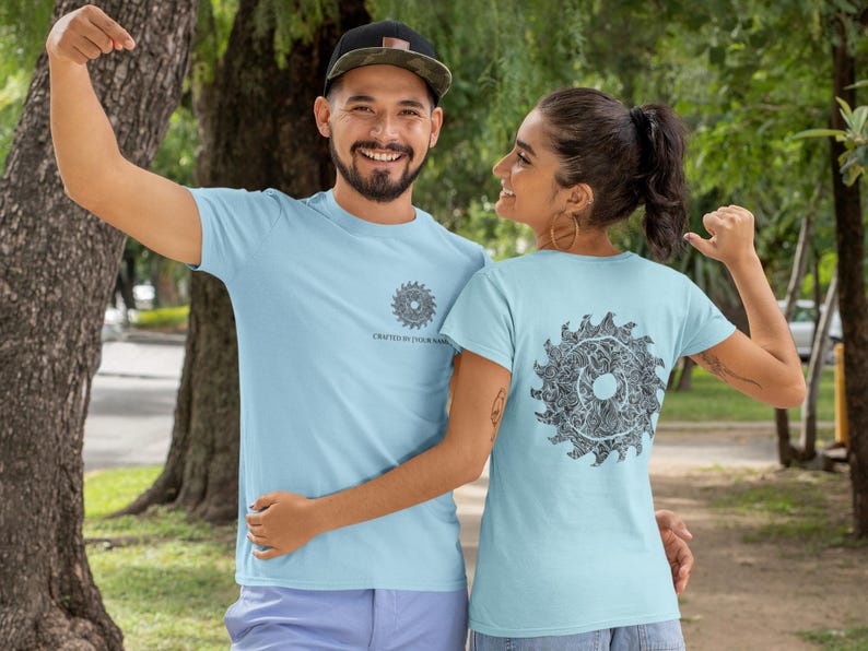 May include: Two people wearing light blue t-shirts with a circular, detailed graphic design. The front of the shirt has a smaller design and the text "CRAFTED BY YOUR NAME". The back of the shirt has a larger version of the design.