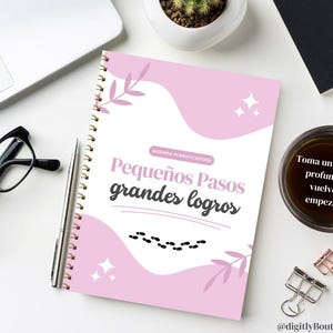 May include: A spiral-bound planner with a pink cover featuring the text "Pequeños Pasos grandes logros" and decorative elements. A cup of coffee, glasses, and a pen are on the white surface. The text "Toma un respiro profundo y vuelve a empezar" is on the coffee.