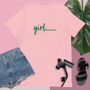 May include: A pink t-shirt with a green graphic that says "girl..."