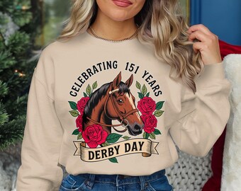 May include: A beige sweatshirt with a brown horse illustration and red roses. The text "Celebrating 151 Years Derby Day" is printed on the sweatshirt.