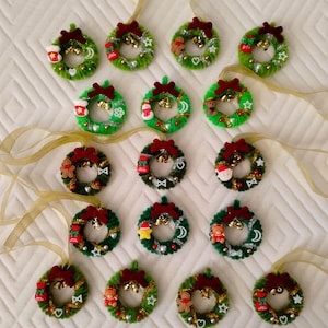 May include: A collection of 18 handmade Christmas wreaths made from green pipe cleaners. Each wreath is decorated with a variety of festive embellishments, including bells, stars, and small figurines.