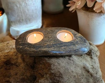 May include: A brown stone candle holder with two lit tea lights. The holder is sitting on a large, rough, brown rock.