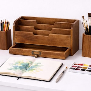 Vintage wooden desk organiser with three tier compartments and open drawer styled as an elegant artist workspace on a white table