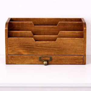 Front view of a vintage wooden desk organiser with three tier compartments and a drawer on a white table