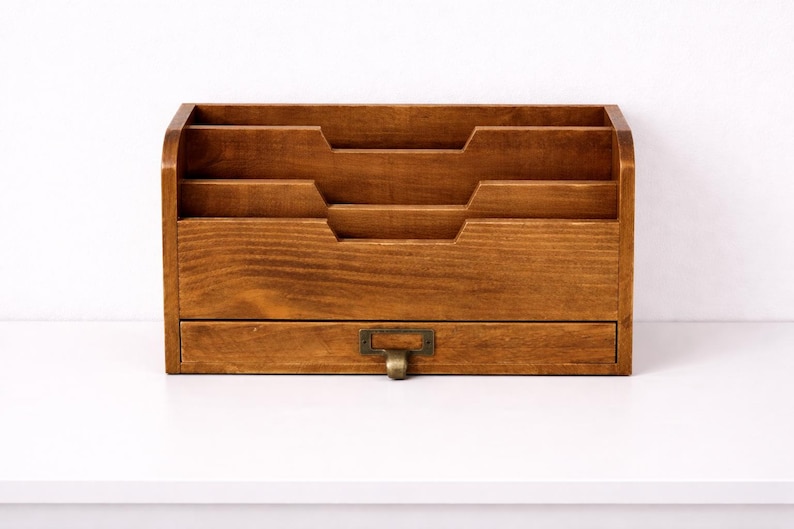 Front view of a vintage wooden desk organiser with three tier compartments and a drawer on a white table