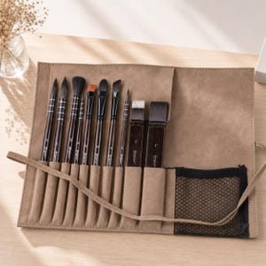 Può includere: Un set di pennelli da artista in una custodia arrotolabile color cuoio. I pennelli hanno manici marrone scuro e varie forme di testina. La custodia ha una tasca a rete e una chiusura con lacci. I pennelli sono disposti in fessure individuali.