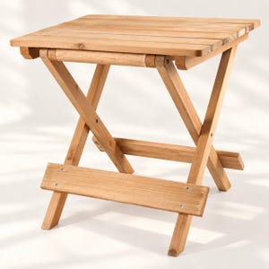 May include: A light brown wooden folding table with a rectangular slatted top and an X-frame base. The structure features a horizontal support bar near the bottom, connected by visible metal screws, providing stability to the collapsible design.