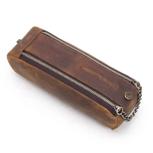 May include: A brown leather pencil case with a zipper closure and a metal chain. The case has the text "COUNTRY SUPPLY" embossed on the front.