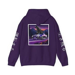 May include: Purple hoodie featuring a graphic of a car driving on a road with a Godzilla-like monster in the background. The text "王と成る" is on the right sleeve and "道は作る" is on the left sleeve.