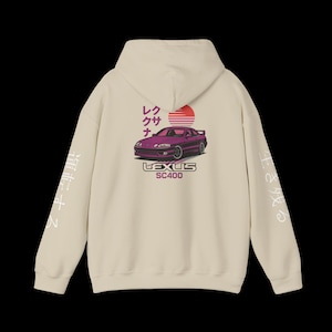 May include: A cream-coloured hoodie with a purple car graphic and a rising sun design. The graphic includes Japanese text and the words "LEXUS SC400". White Japanese text is printed on the sleeves.