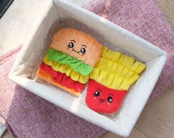 May include: A white storage basket with a polka dot pattern contains two plush toys shaped like a hamburger and french fries. The hamburger has a smiling face and is layered with green lettuce, yellow cheese, and red tomato. The french fries have a smiling face and are yellow.