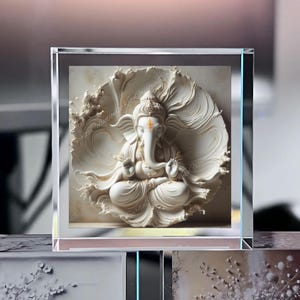 May include: A white sculpture of the Hindu deity Ganesha, seated in a lotus position, encased in a clear glass block. The sculpture features intricate details and is set against a textured background. The text "Sarita Collection Koby Creative Co" is visible.
