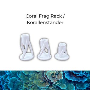 Pode incluir: Três suportes brancos para fragmentos de coral de tamanhos variados. Cada suporte tem uma base circular e um design torcido com a parte superior aberta. O texto "Coral Frag Rack / Korallenständer" está acima.