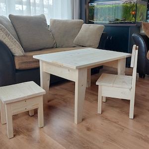 Può includere: Un set di mobili in legno per bambini, composto da un tavolo e due sedie. Il tavolo e le sedie sono realizzati in legno grezzo e hanno un design semplice e moderno.