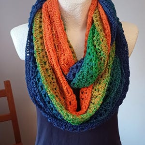 Puede incluir: Bufanda infinita hecha a mano en un vibrante arcoíris de colores, incluyendo naranja, verde y azul. La bufanda está tejida a ganchillo con un diseño de tejido abierto y se muestra en un maniquí. Un accesorio perfecto para cualquier atuendo.