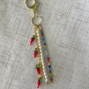 May include: A gold keychain with a red chili pepper charm, white pearl beads, and colorful beaded strands.