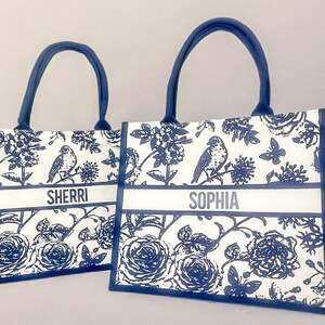 May include: Two blue and white tote bags with floral and bird designs. The bags have personalized names, "Sherri" and "Sophia", printed on the front.